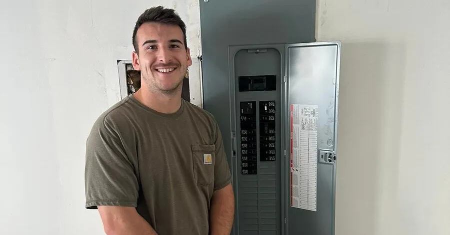 Electrician standing beside the newly installed panel at the end of a service upgrade
