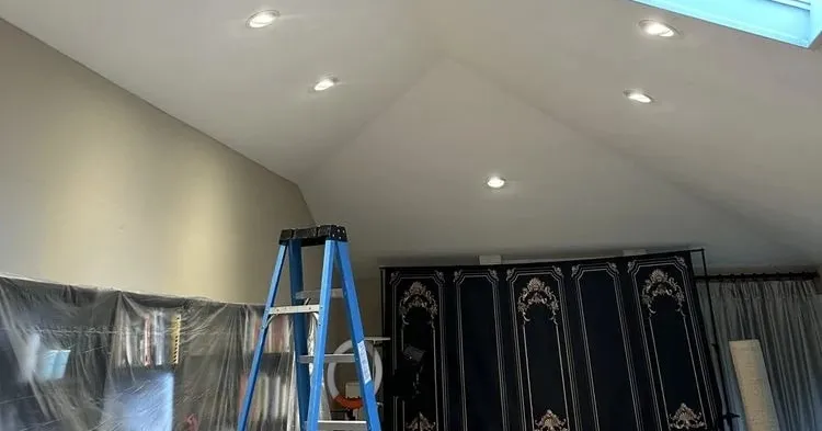 Newly installed recessed lights in a finished ceiling, with a ladder still in the room