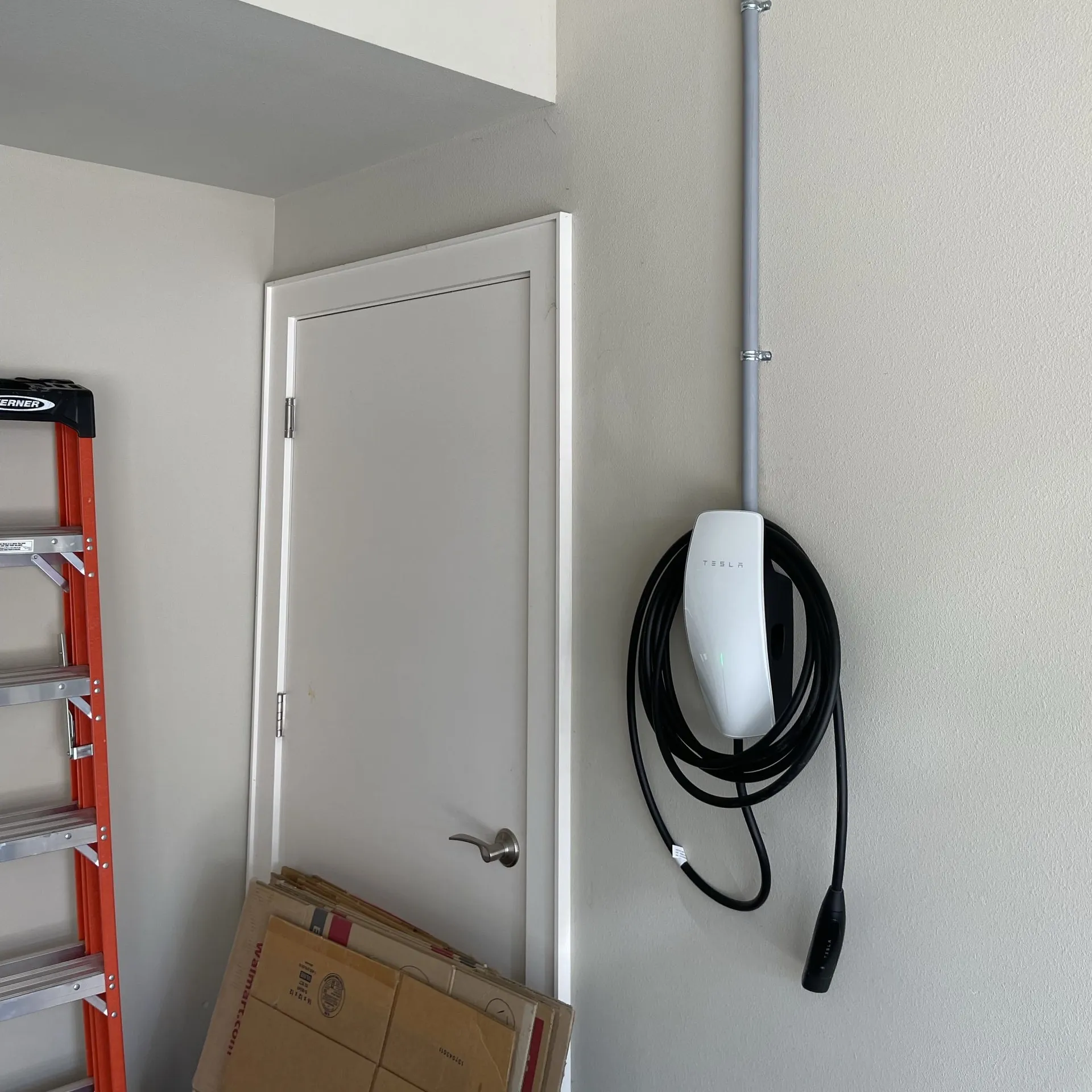 Tesla Wall Connector in a garage with a conduit run across to the panel on the far wall