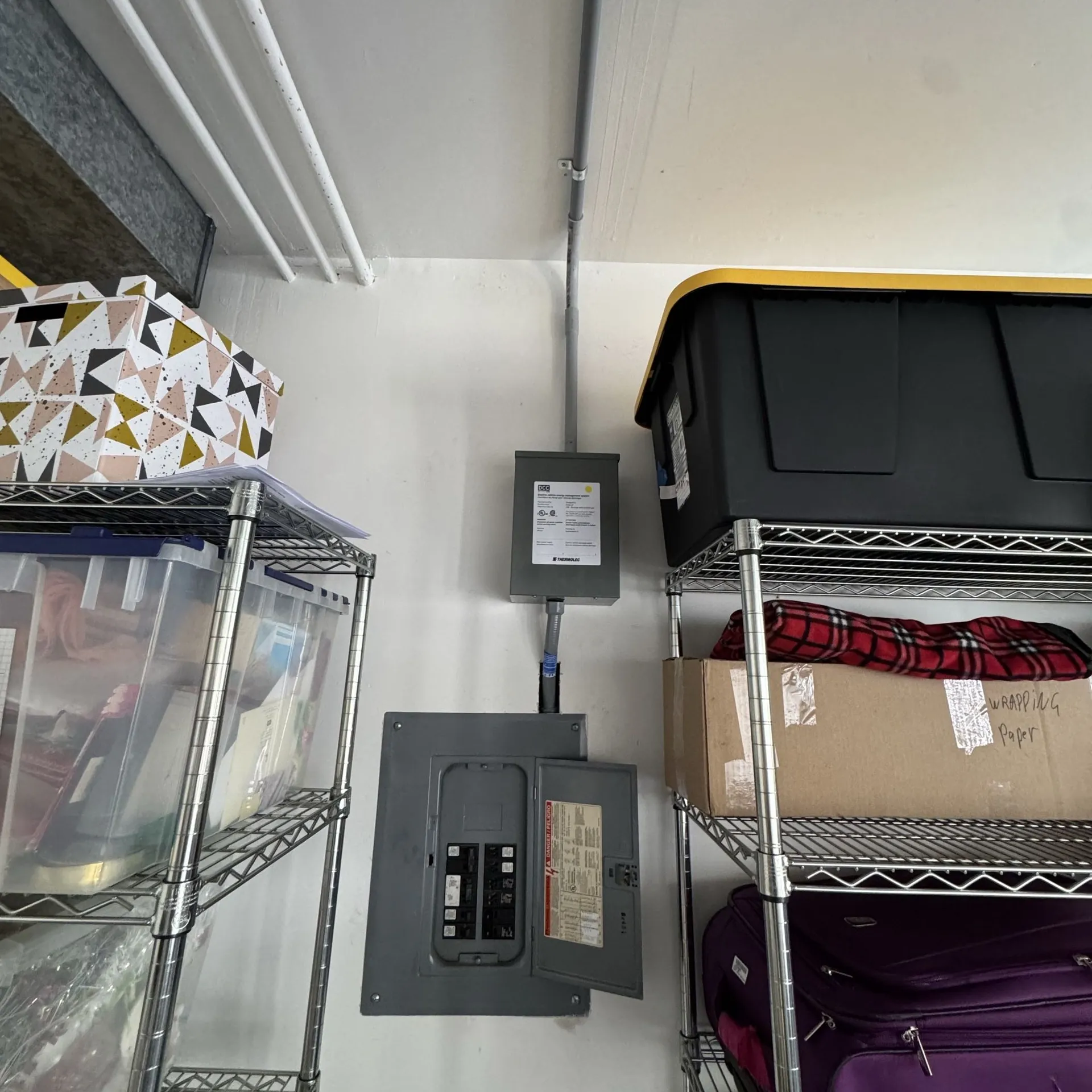 Load shedding device mounted above a garage sub panel, with conduit running up to the ceiling