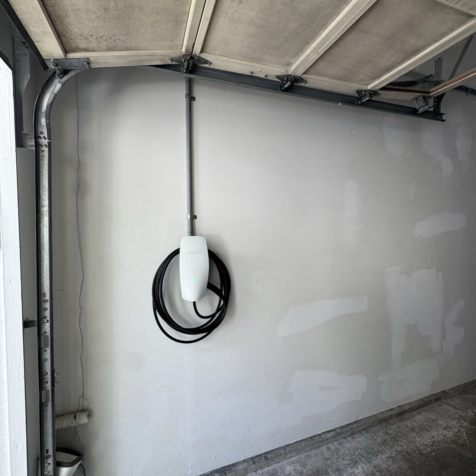 Tesla Wall Connector on the far garage wall, fed by a conduit run dropping from the ceiling