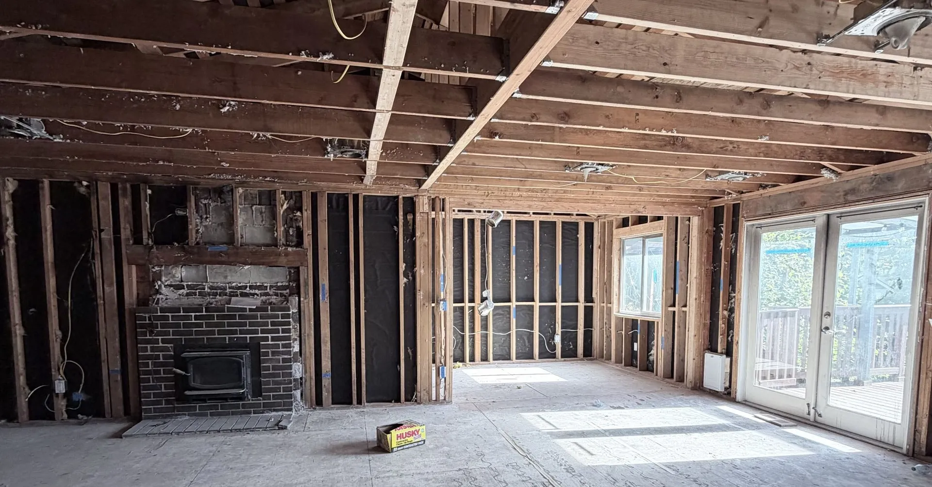 Living room stripped back to the framing around the fireplace, with the carpet, drywall and old wiring pulled out