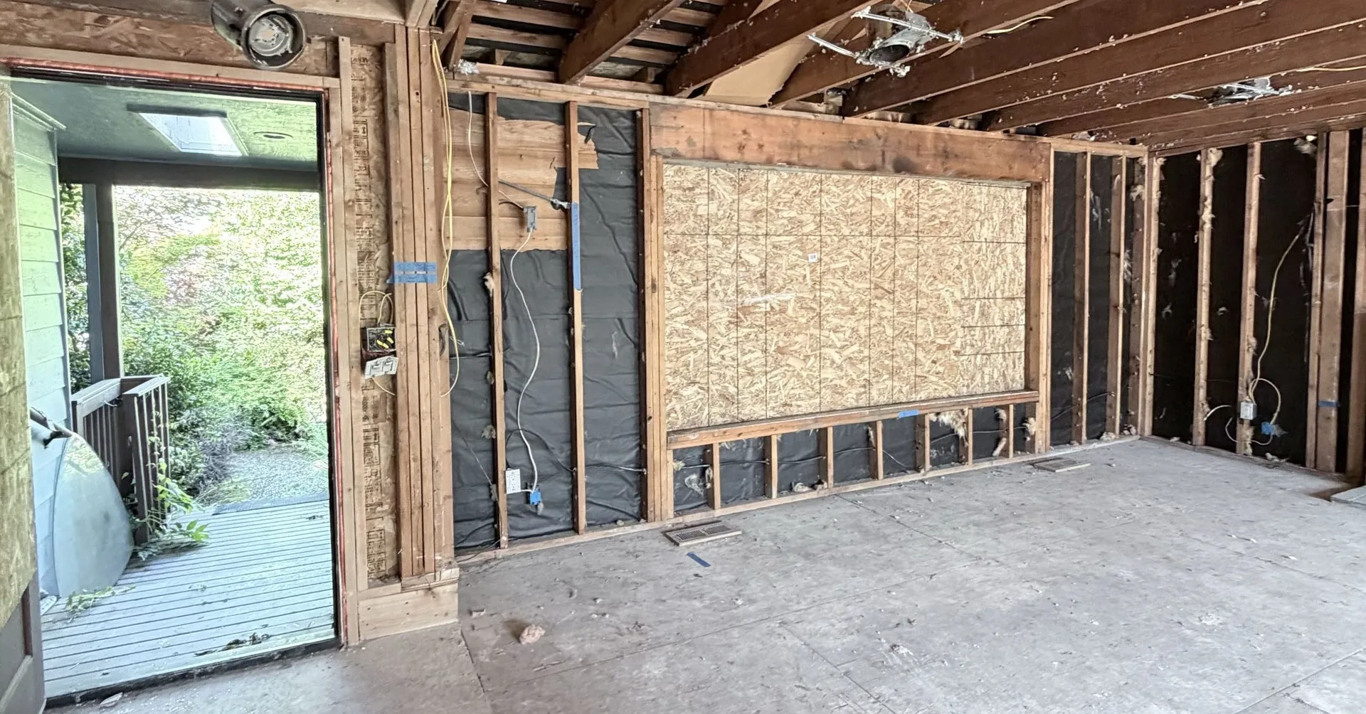 Entry room stripped and staged for a rewire, with the drywall and carpet out and the window boarded over