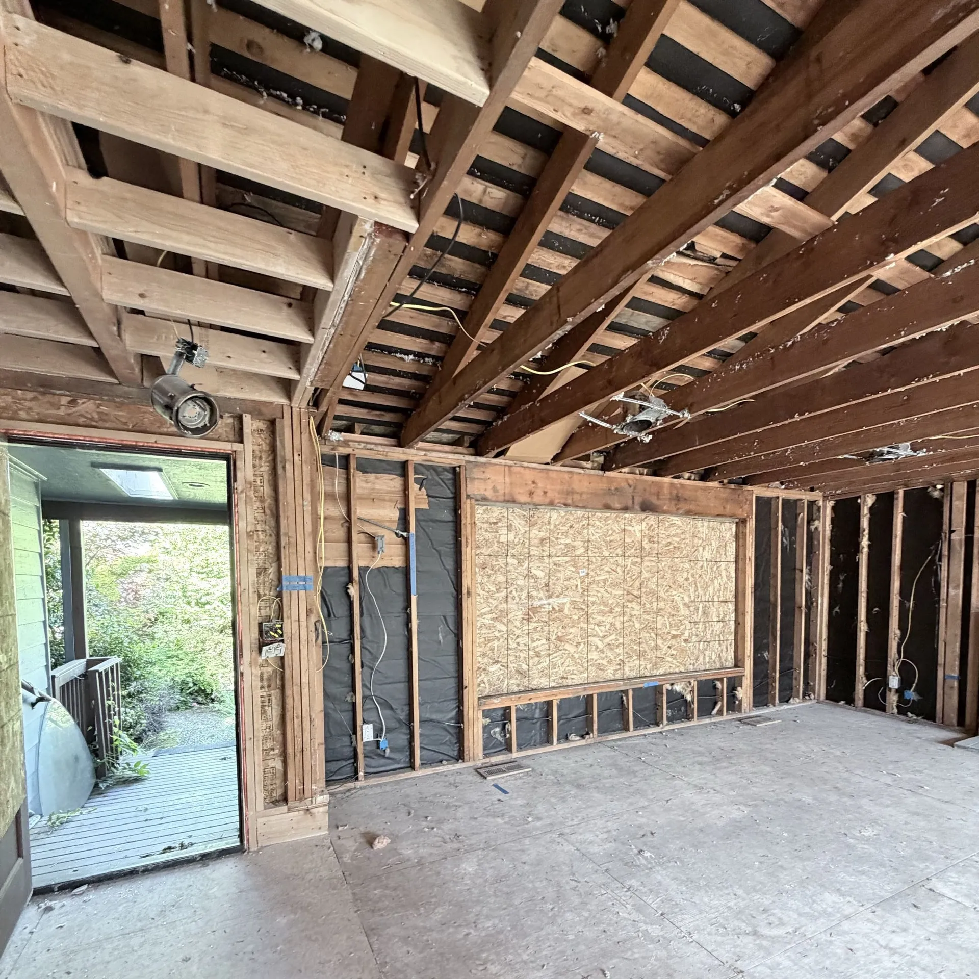Entry room stripped and staged for a rewire, with the drywall and carpet out and the window boarded over