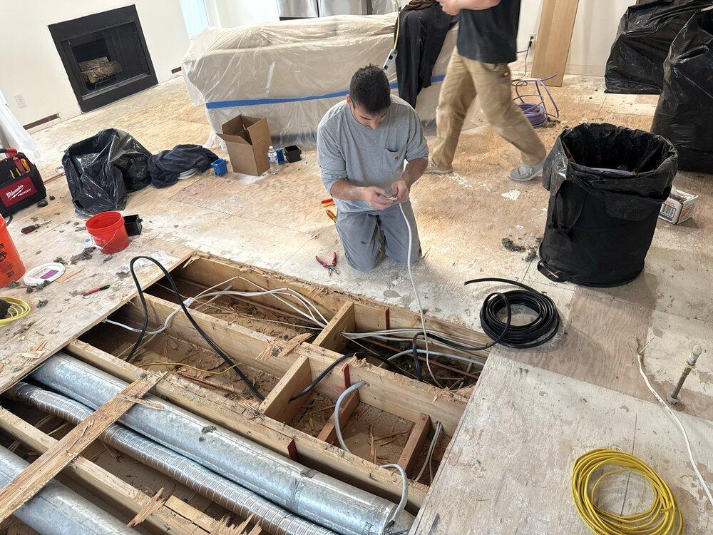 Electrician running new wiring through open floor joists during a home remodel